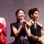 Seorang aktris memegang mikrofon di atas panggung acara film, diapit dua pemeran lainnya