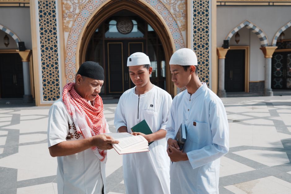 Sekelompok pria mempelajari teks keagamaan di luar masjid di Indonesia