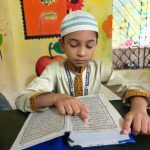 Seorang anak laki-laki berpakaian tradisional membaca kitab di dalam kelas