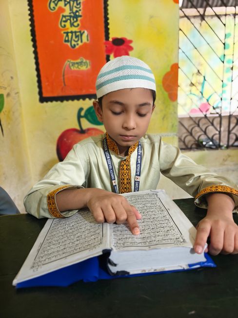 Seorang anak laki-laki berpakaian tradisional membaca kitab di dalam kelas