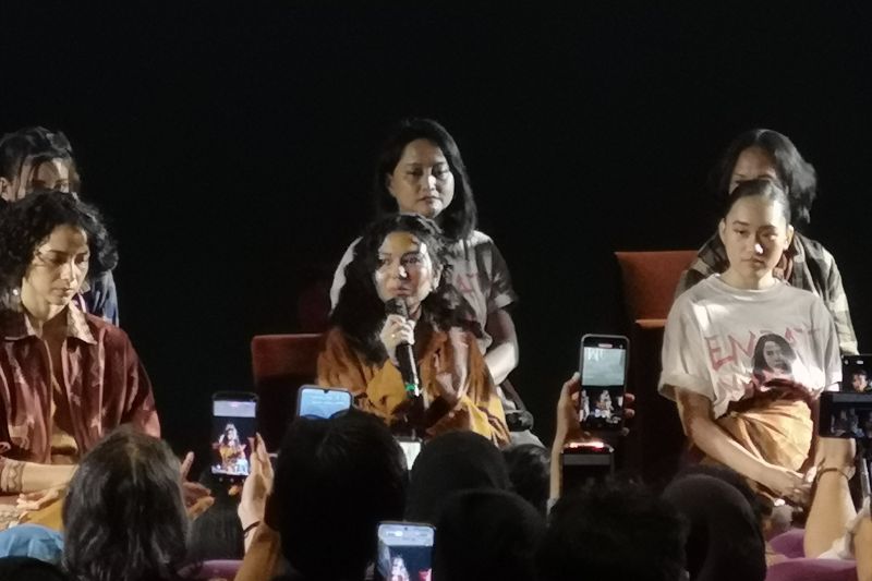 Para pemain dan kru film duduk di atas panggung acara, seorang perempuan memegang mikrofon di hadapan penonton