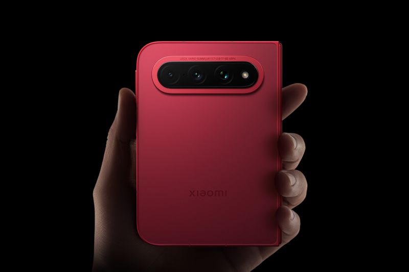 Ponsel Xiaomi berwarna merah dipegang tangan dengan latar hitam