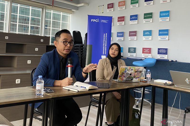 Seorang pria berbicara dengan mikrofon dalam sebuah diskusi di depan spanduk FPCI