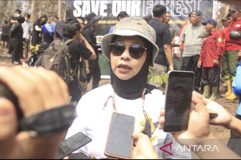 Seorang perempuan berbicara kepada wartawan di depan spanduk bertuliskan Save Our Forest