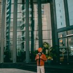A fashionable adult stands outside a modern building in Jaipur, India, exuding confidence.