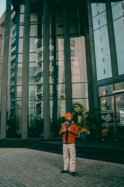 A fashionable adult stands outside a modern building in Jaipur, India, exuding confidence.