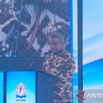 Seorang pejabat berbatik berbicara di podium dalam sebuah acara, dengan layar besar di belakangnya