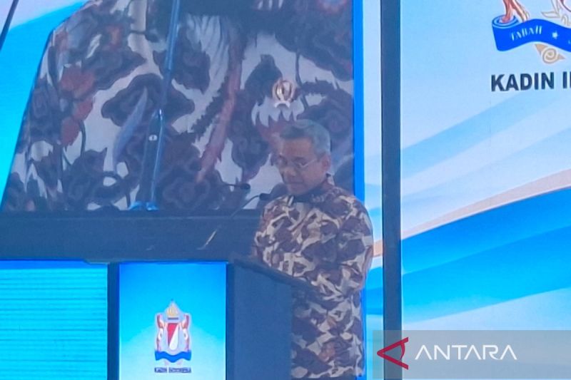 Seorang pejabat berbatik berbicara di podium dalam sebuah acara, dengan layar besar di belakangnya