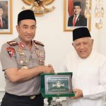 Kapolri berseragam polisi dan Ketua Umum PBNU berbaju putih memegang plakat hijau bersama di dalam ruangan