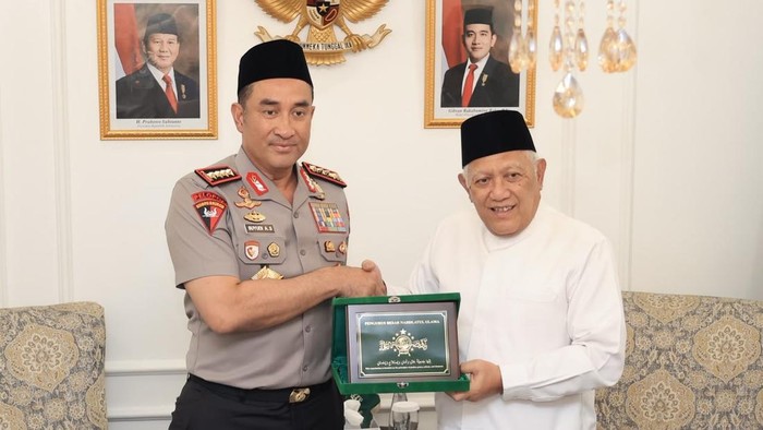 Kapolri berseragam polisi dan Ketua Umum PBNU berbaju putih memegang plakat hijau bersama di dalam ruangan