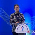 Menteri Kesehatan berbaju batik bunga berbicara di podium berlogo Konsil Kesehatan Indonesia dengan latar biru