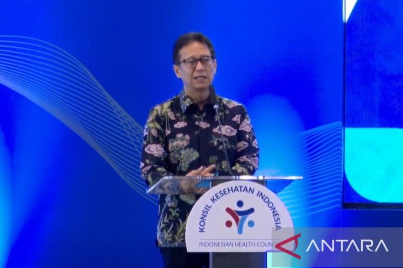 Menteri Kesehatan berbaju batik bunga berbicara di podium berlogo Konsil Kesehatan Indonesia dengan latar biru