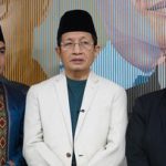 Tiga pria berdiri berdampingan, pria di tengah memakai jas putih dan peci hitam