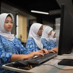 Siswi berseragam biru bermotif dan berjilbab putih mengerjakan tes di depan komputer