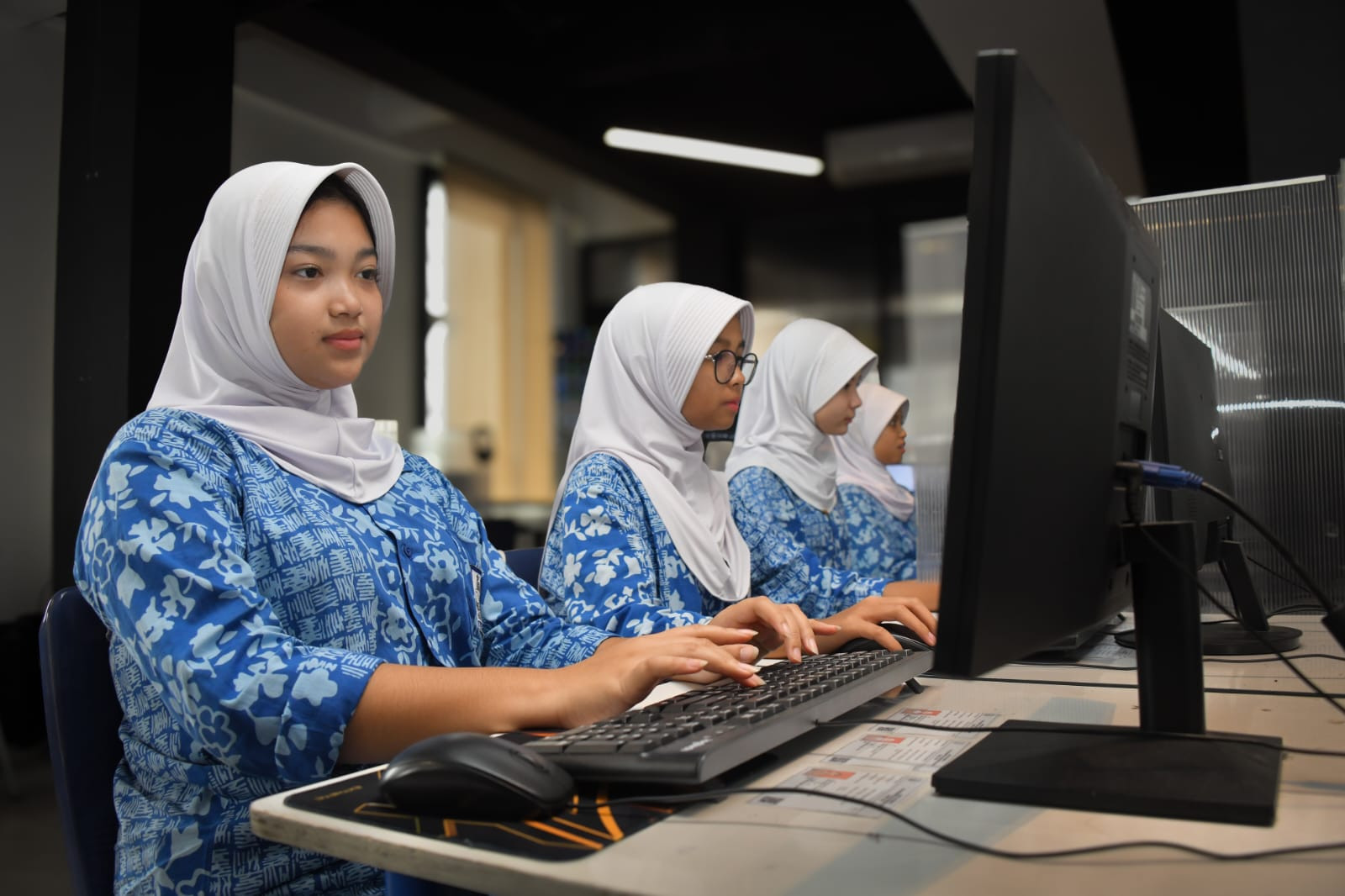 Siswi berseragam biru bermotif dan berjilbab putih mengerjakan tes di depan komputer