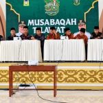 Peserta MTQ duduk di meja dengan latar spanduk Musabaqah Tilawatil Quran