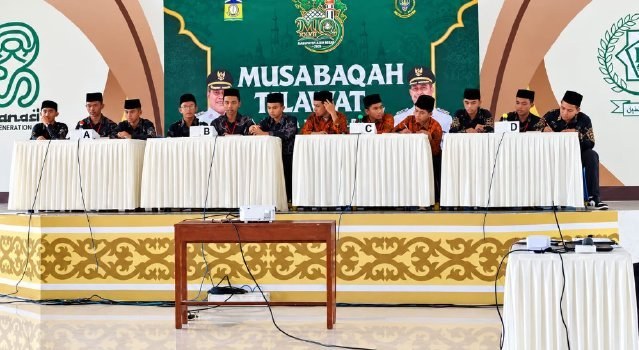 Peserta MTQ duduk di meja dengan latar spanduk Musabaqah Tilawatil Quran