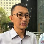 Seorang pria berkacamata berkemeja putih memberikan keterangan kepada wartawan di luar sebuah gedung bertingkat