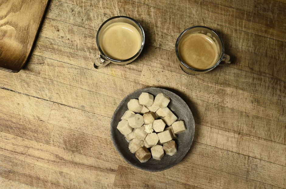 Dua cangkir espresso dan semangkuk gula batu di atas meja kayu