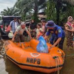 Petugas dan warga di sekitar perahu karet oranye BNPB di jalan tergenang banjir di Aceh Selatan