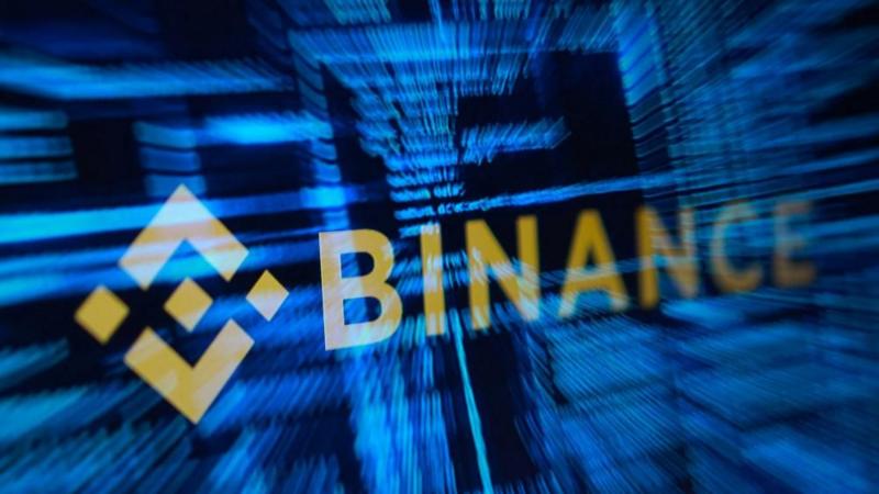 Logo Binance berwarna emas di atas latar digital biru gelap