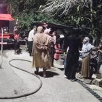 Truk tangki air merah di malam hari dengan warga berkumpul di sekitarnya saat penyaluran air bersih