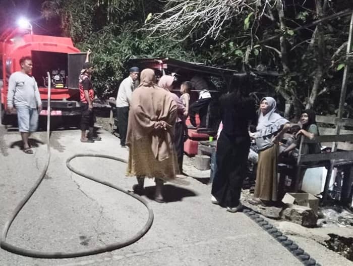 Truk tangki air merah di malam hari dengan warga berkumpul di sekitarnya saat penyaluran air bersih