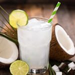 Segelas air kelapa segar dengan es dan buah kelapa muda di atas meja