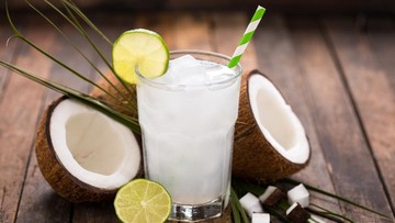 Segelas air kelapa segar dengan es dan buah kelapa muda di atas meja