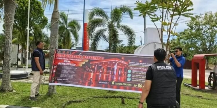 Personel Polres Aceh Jaya memasang spanduk imbauan penertiban BBM subsidi di SPBU