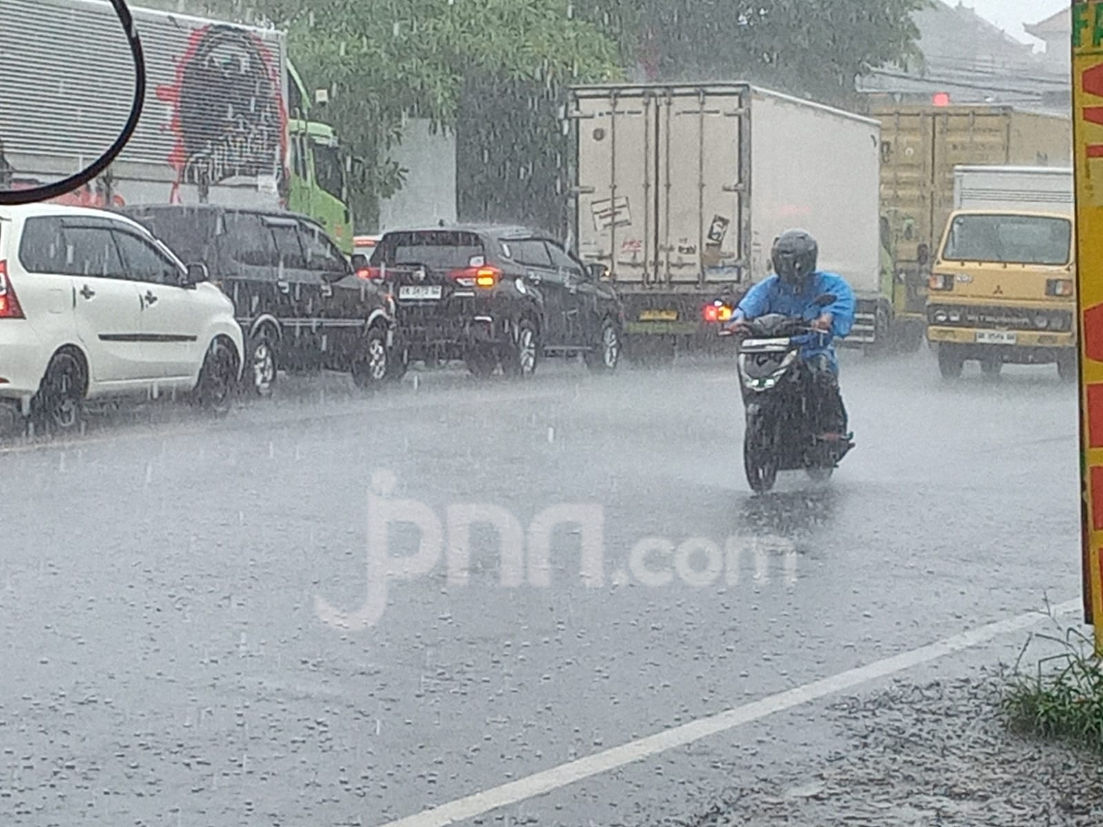 Pengendara memakai jas hujan melintas di jalan saat hujan di Bali