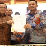 Dua pria berbatik memegang dokumen dalam sebuah acara seremonial