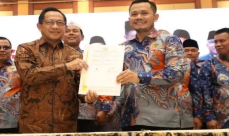 Dua pria berbatik memegang dokumen dalam sebuah acara seremonial