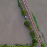 Jalan yang tergenang banjir dilihat dari udara, dikelilingi air dan pepohonan hijau
