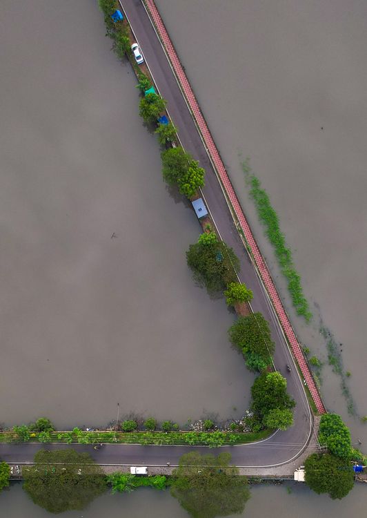 Jalan yang tergenang banjir dilihat dari udara, dikelilingi air dan pepohonan hijau