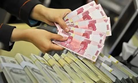 Petugas menunjukkan uang rupiah dan dolar Amerika Serikat