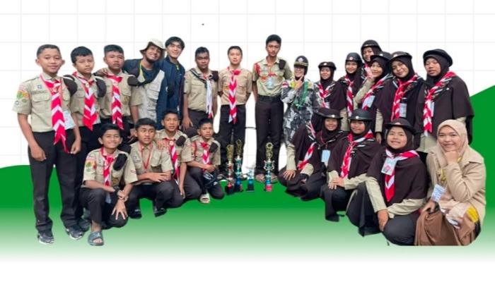Foto bersama siswa pramuka berseragam krem dan hasduk merah putih dengan deretan piala di depan mereka