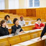 Dosen berdiri di depan mahasiswa dalam ruang kuliah universitas