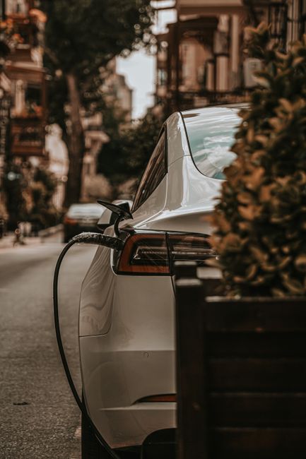 Mobil listrik berwarna putih sedang mengisi daya di stasiun pengisian kendaraan listrik di jalan kota