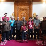 Foto bersama sekelompok orang di ruangan berkarpet merah, seorang perempuan berkursi roda di barisan depan