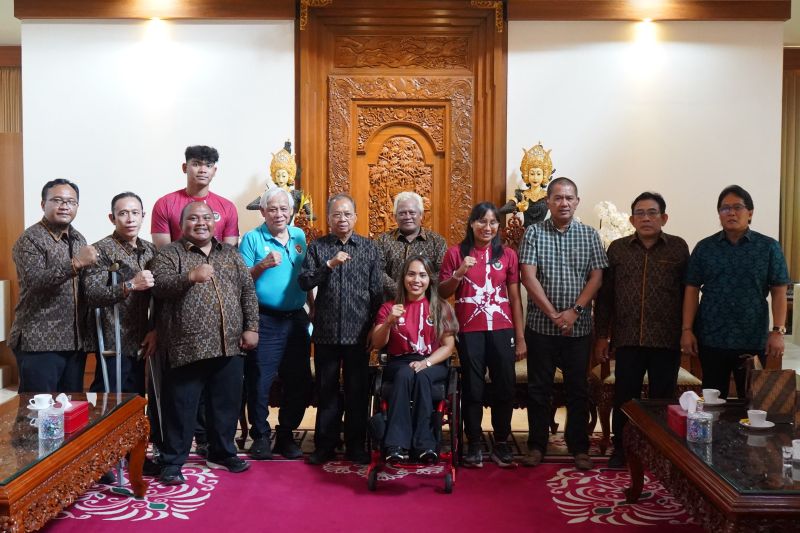 Foto bersama sekelompok orang di ruangan berkarpet merah, seorang perempuan berkursi roda di barisan depan