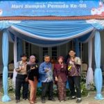 Lima anak muda berpose di bawah tenda biru dengan spanduk Upacara Peringatan Hari Sumpah Pemuda Ke-98