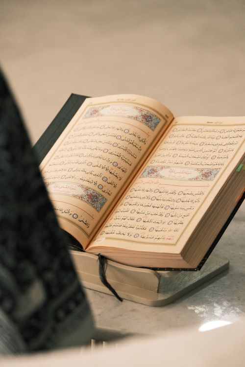 Al-Qur'an terbuka di atas rehal kayu dengan kaligrafi Arab yang indah