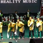 Para penampil muda berbaju adat kuning menari dan bermain musik tradisional di atas panggung