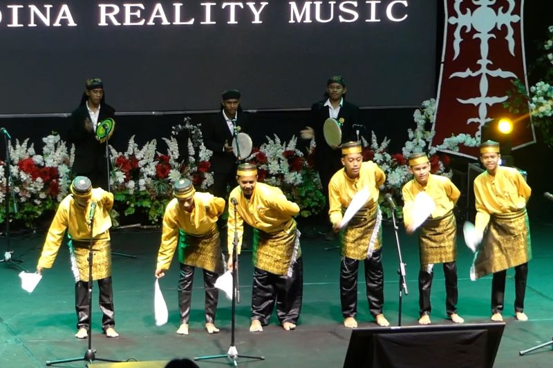 Para penampil muda berbaju adat kuning menari dan bermain musik tradisional di atas panggung