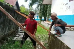 Dua warga menangani pagar sekolah yang miring di SMPN 2 Kluet Utara