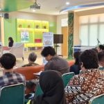 Suasana sosialisasi di sebuah ruangan, sejumlah peserta duduk menyimak pemateri di panggung