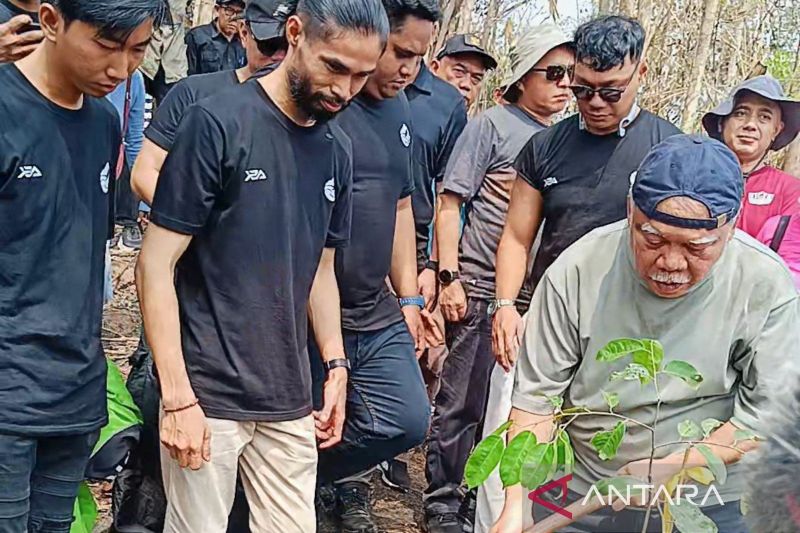 Seorang pria menanam bibit pohon di lahan bekas kebakaran disaksikan sejumlah pemuda