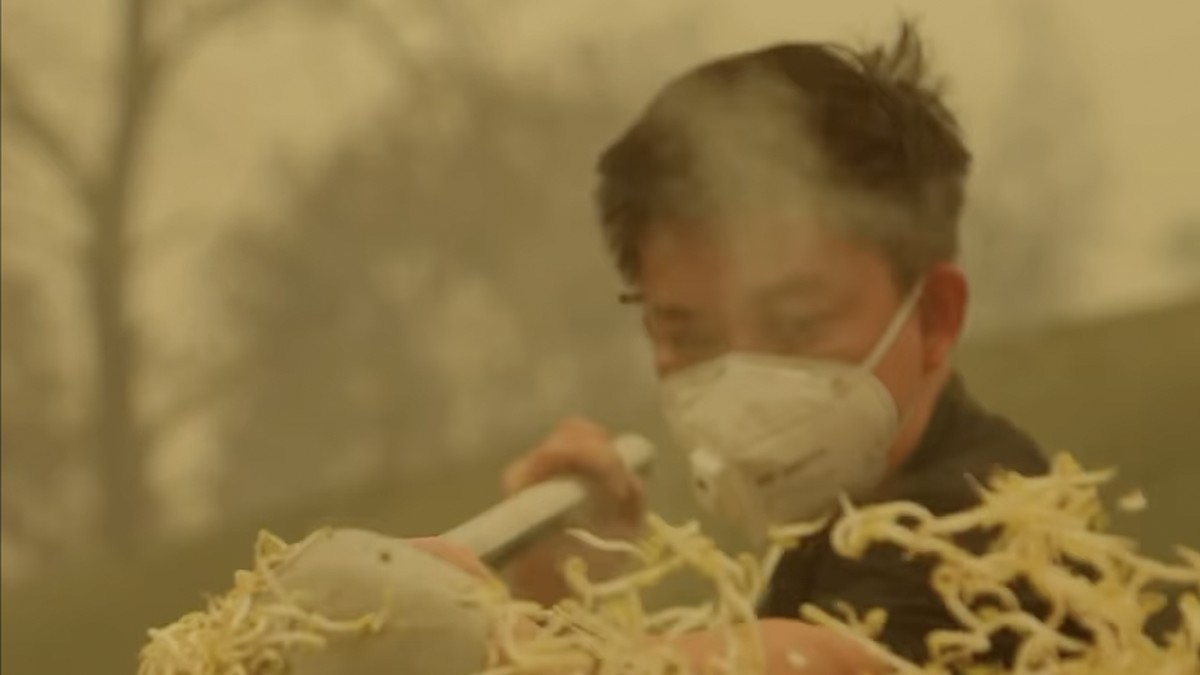 Pria bermasker memasak dalam kuali besar di tengah udara berasap
