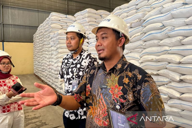 Pejabat Bulog berhelm putih menjelaskan di depan tumpukan karung beras di gudang Semarang